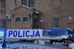 fragment policyjnego radiowozu na tle Oddziału Zewnętrznego w Szczytnie Aresztu Śledczego w Olsztynie