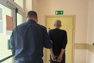 Policjant doprowadzający zatrzymanego mężczyznę